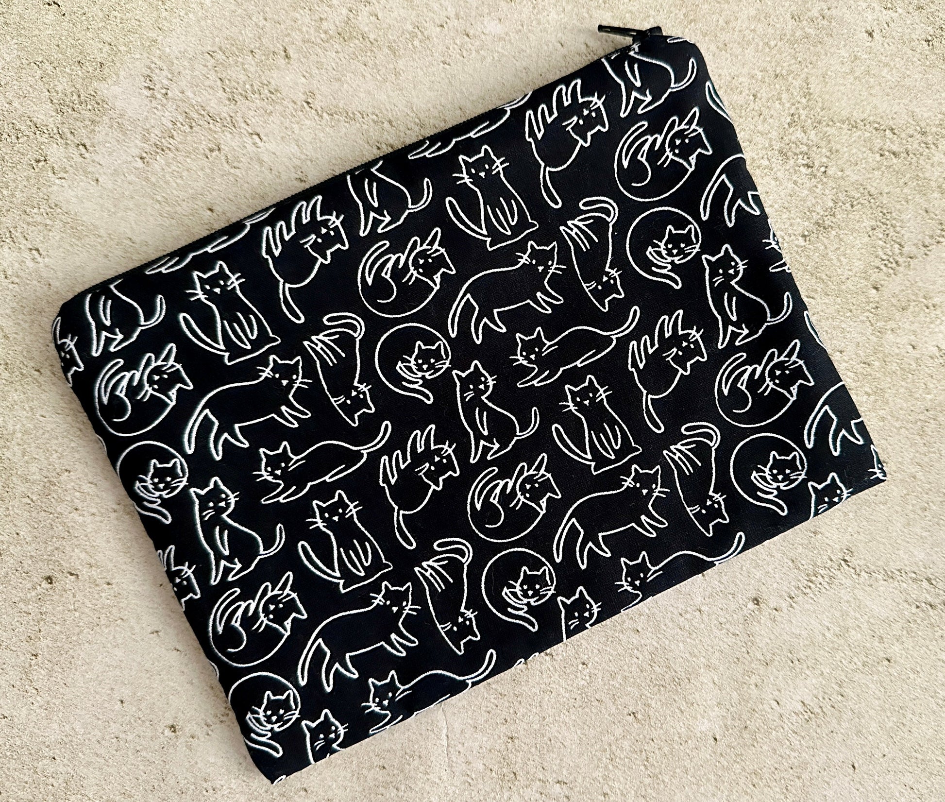 Black pouch with white cat pattern on a beige surface