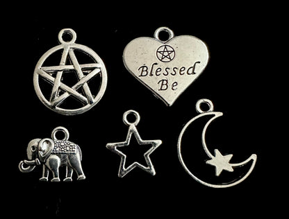 Set of silver charms including a pentagram, heart with 'Blessed Be' text, elephant, star, and moon on a black background.