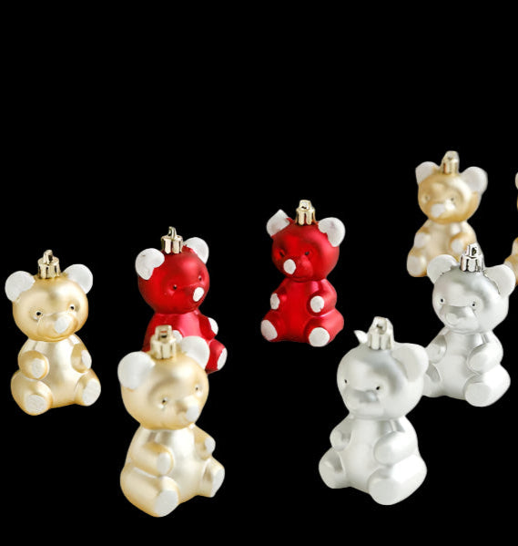 Decorative bear ornaments in red, gold, and silver on a white surface with a Christmas tree and decorations in the background.