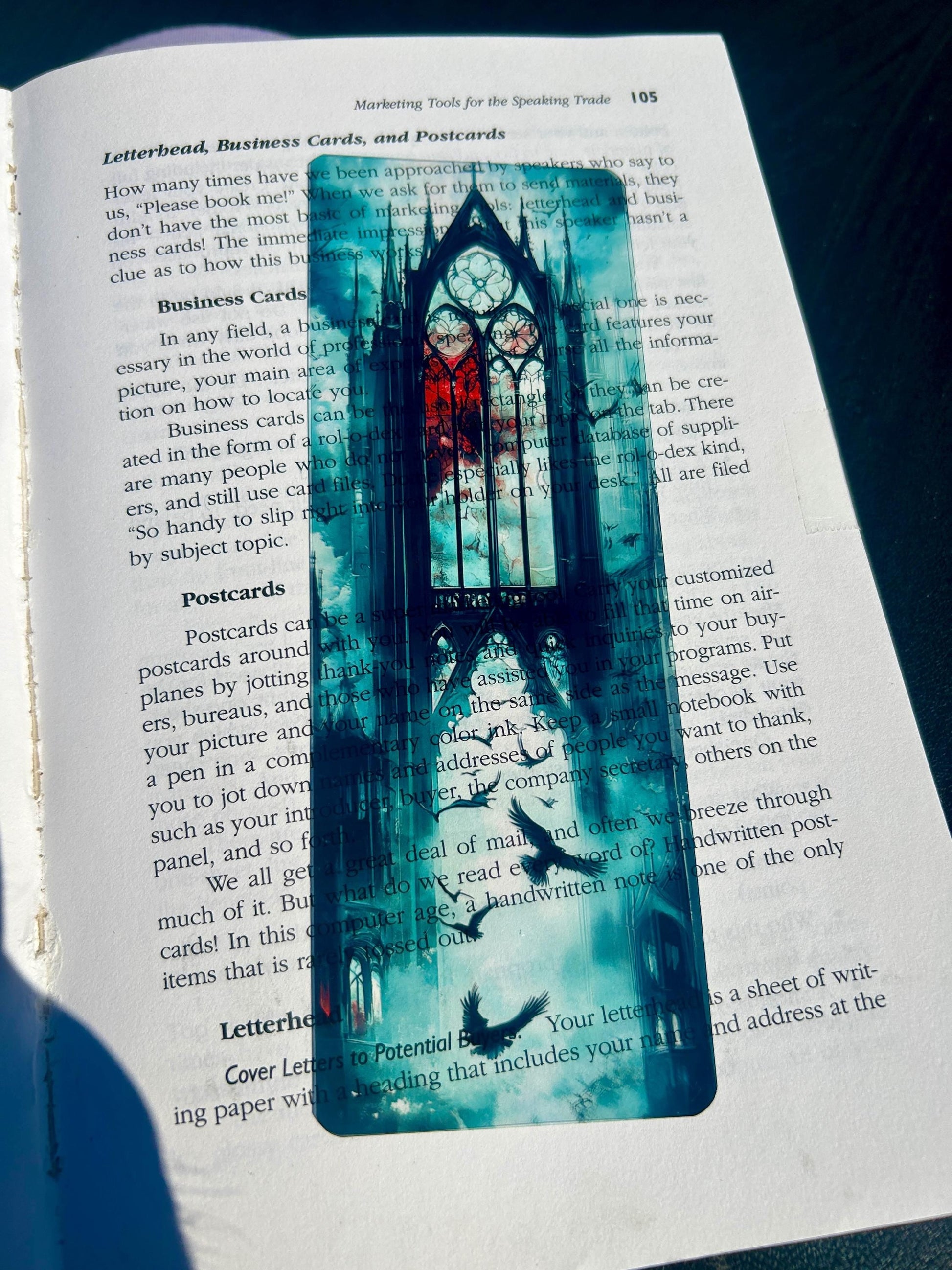 A rectangular acrylic bookmark with a gothic tree illustration, resting on an open book page.