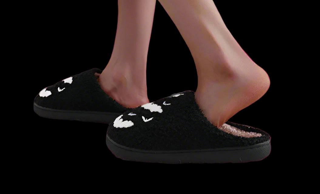 Person wearing black slippers with white paw prints on a light-colored floor.