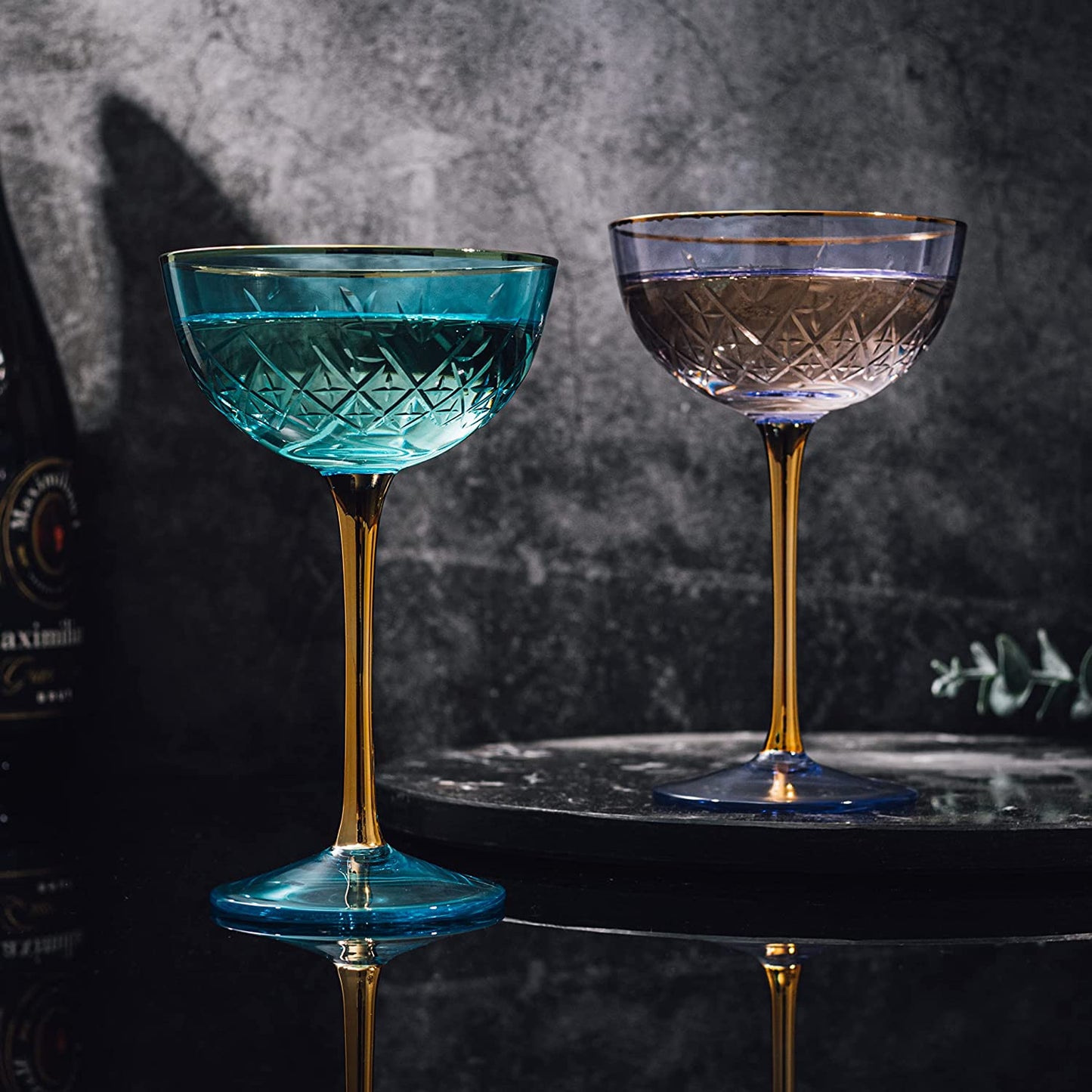Two cocktail glasses with blue and purple drinks on a dark surface.