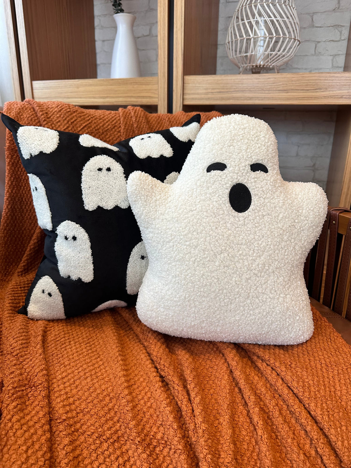 Two ghost-themed pillows on an orange surface with a wooden shelf in the background.