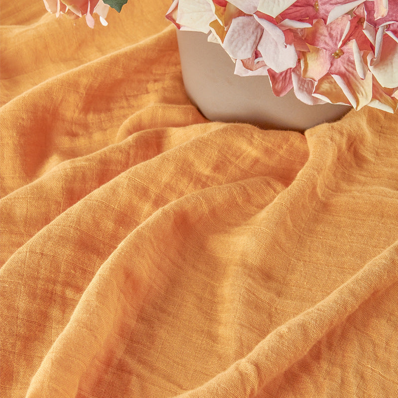 Close-up of orange fabric with a vase and flowers in the background