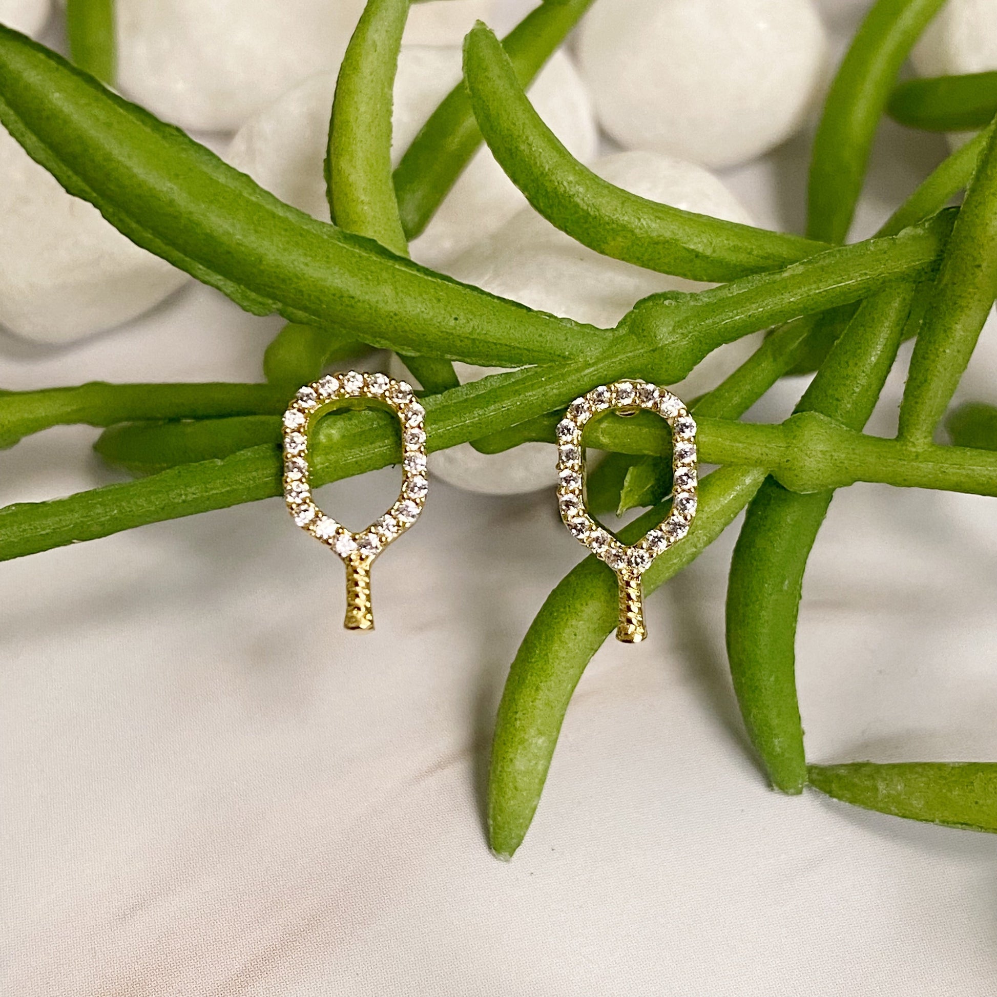 Gold earrings with gemstones on green leaves