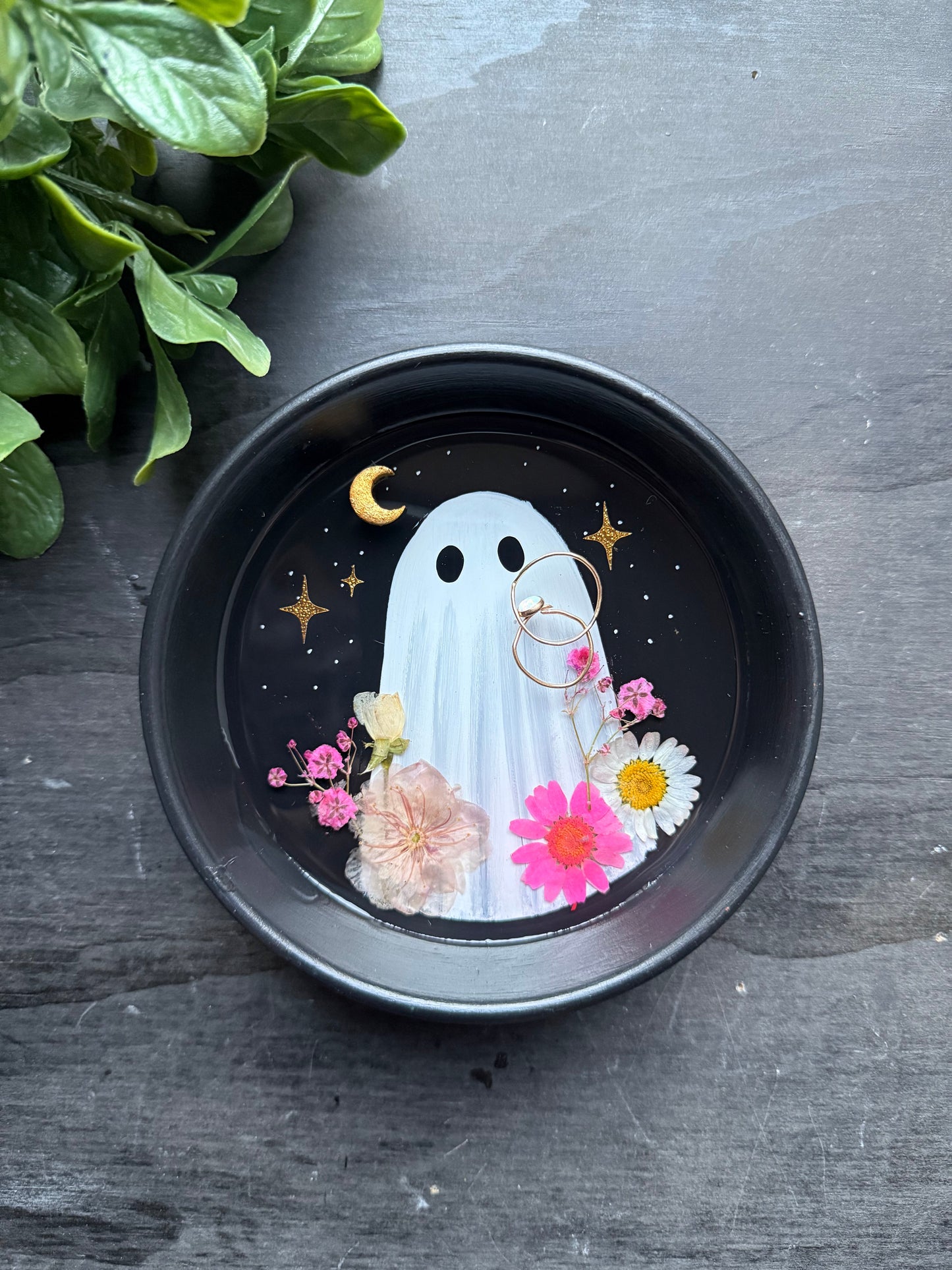 Decorative plate with a ghost design surrounded by flowers on a dark surface.