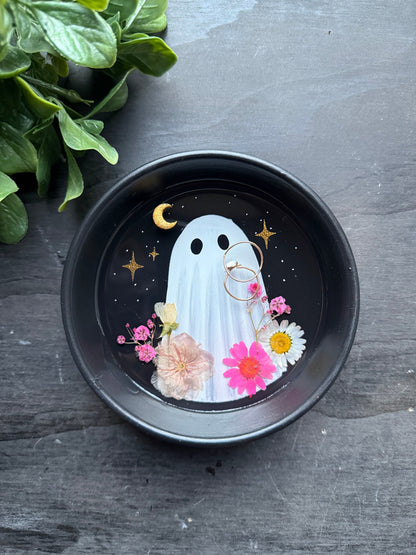 Decorative plate with a ghost design surrounded by flowers on a dark surface.