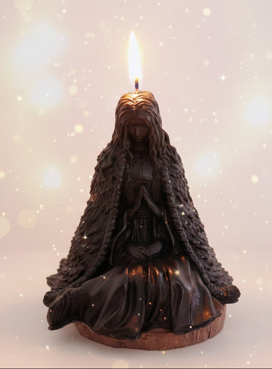 Black figurine of a hooded figure with a lit candle on a surface with blurred background