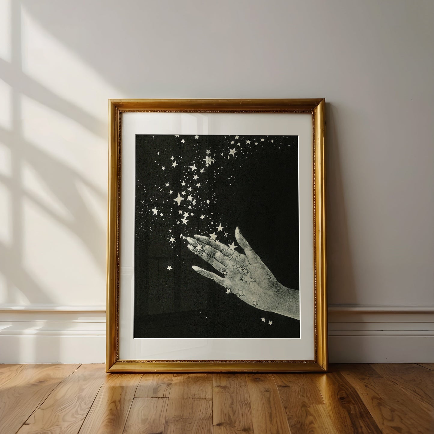 Framed artwork of a hand holding stars on a black background, leaning against a wall.