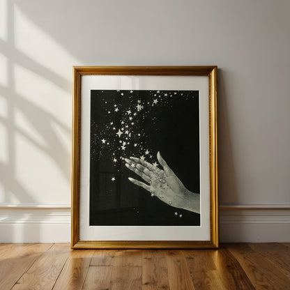 Framed artwork of a hand holding stars on a black background, leaning against a wall.