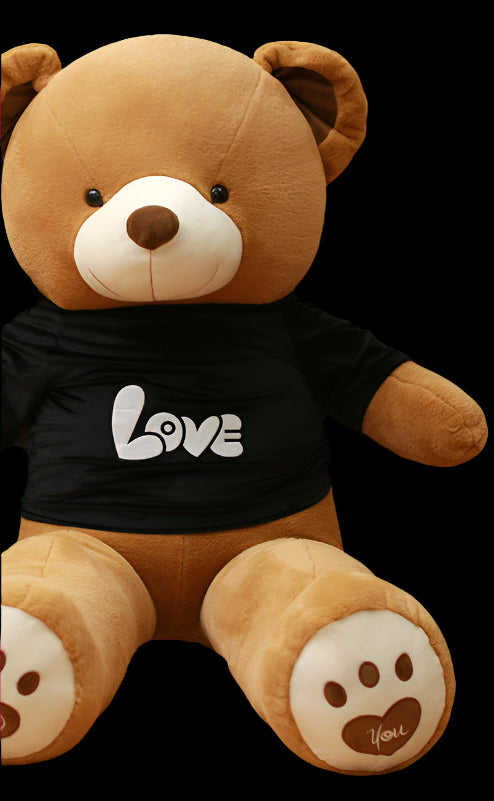 Large brown teddy bear with a black shirt that says 'LOVE' held by a person in front of a bookshelf.