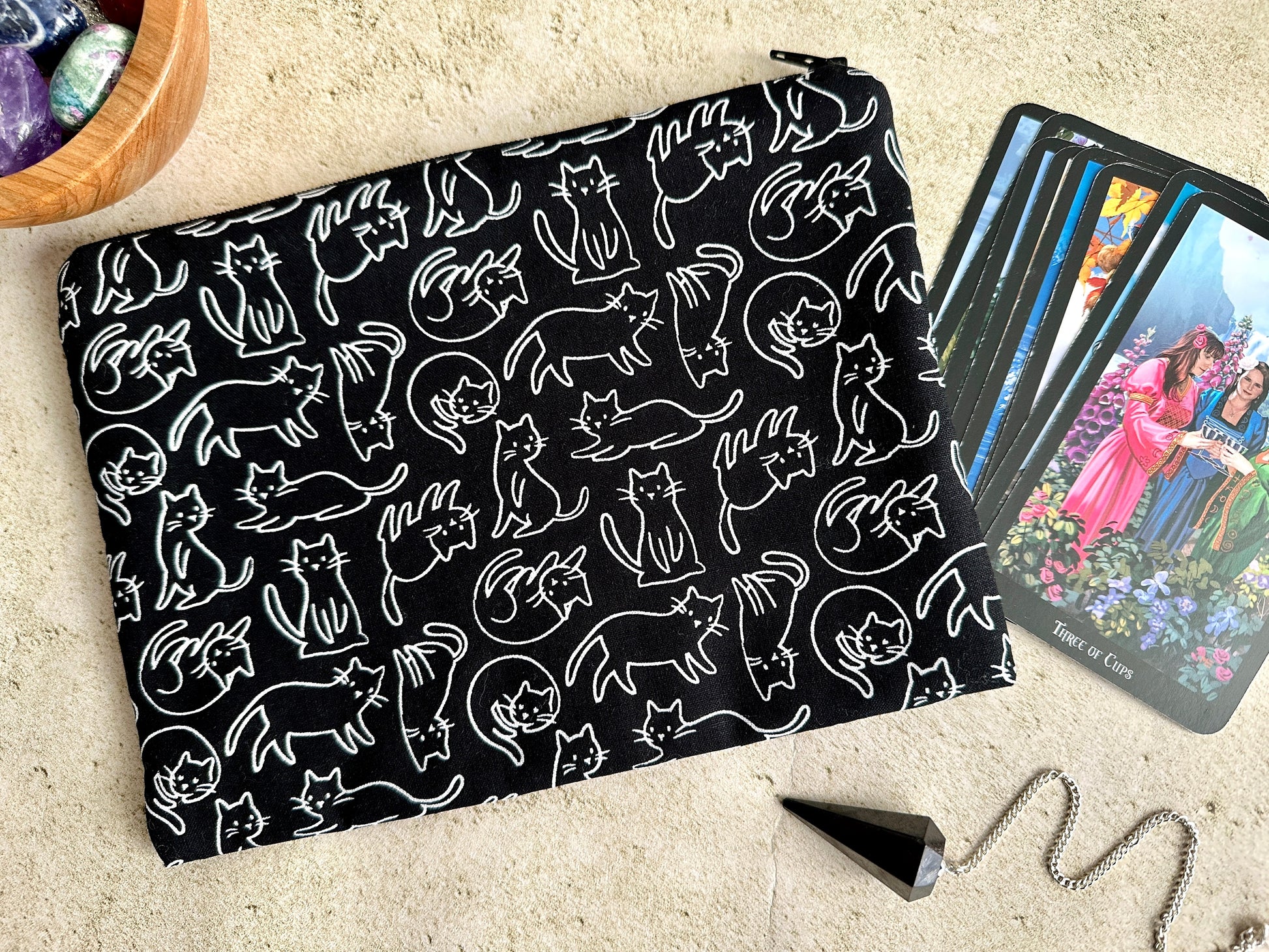 Black pouch with white cat pattern next to tarot cards on a beige surface