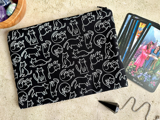 Black pouch with white cat pattern next to tarot cards on a beige surface