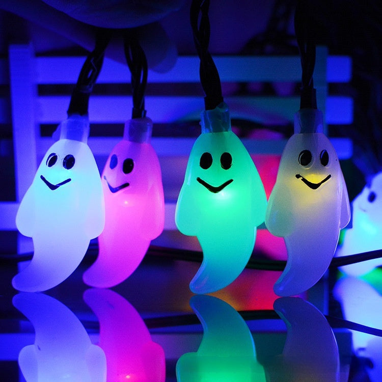 String lights shaped like ghosts in white, pink, green, and blue on a reflective surface.