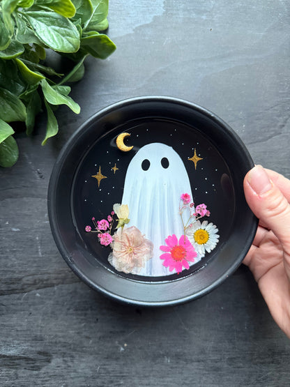 Black bowl with a ghost design and flowers on a dark surface