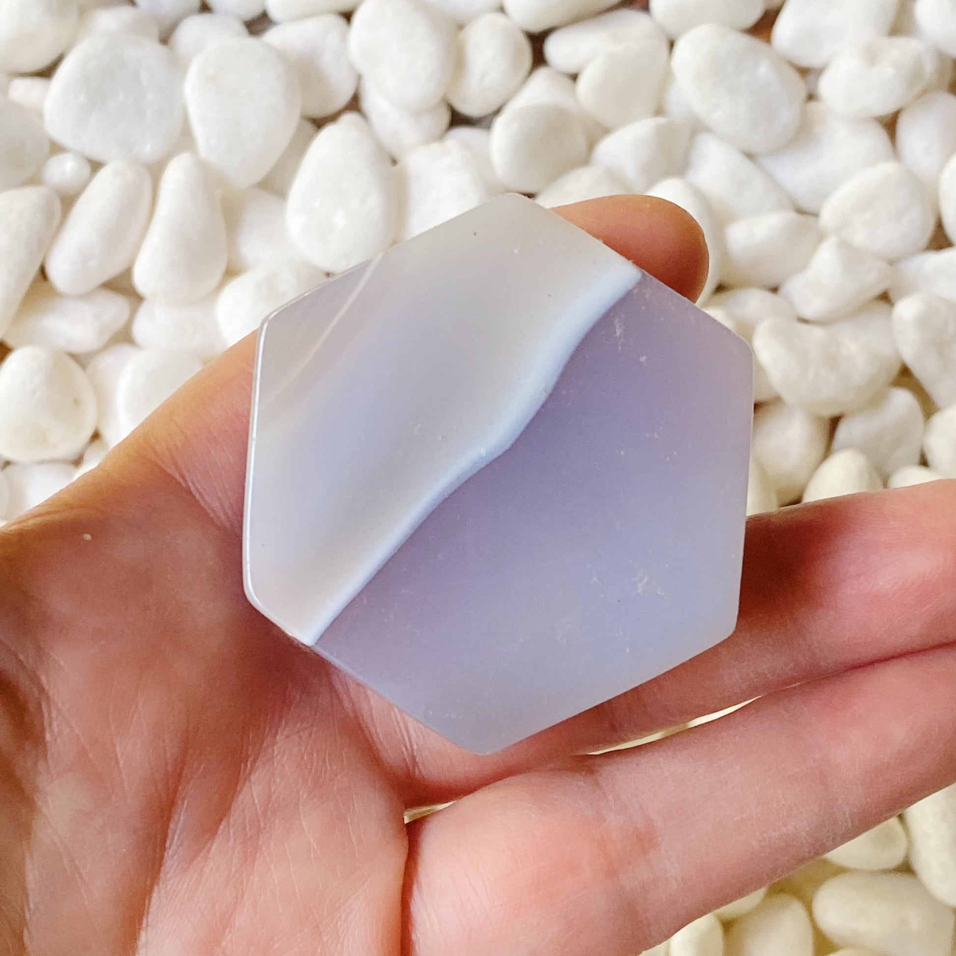 Hand holding a geometric crystal-like stone against a background of white pebbles.