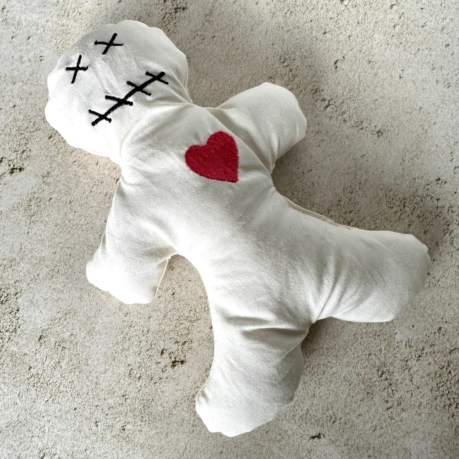 White plush toy with red heart and black crosses on a textured surface