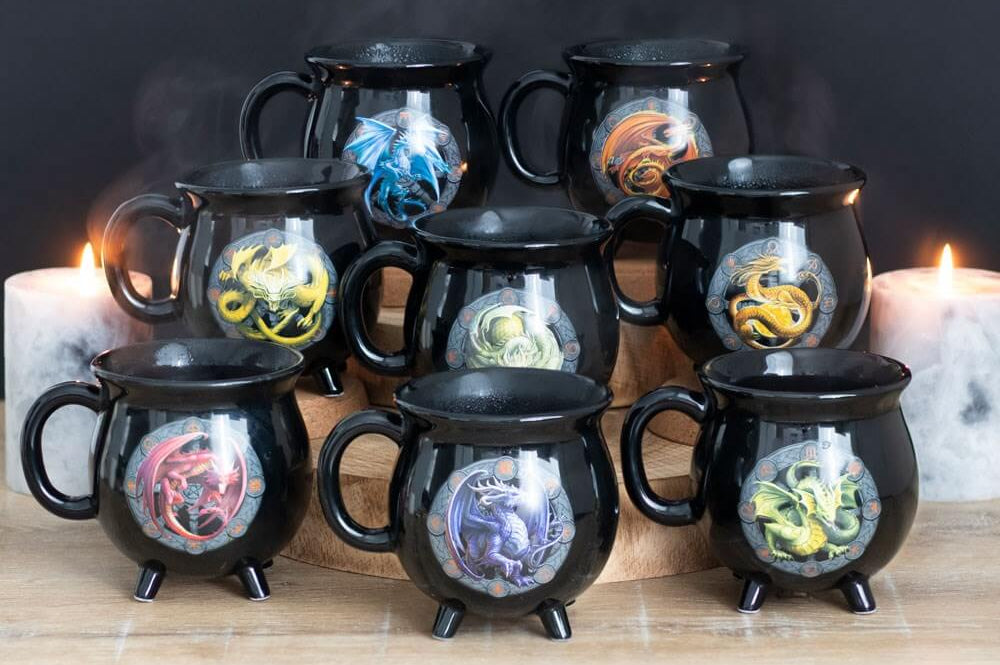 Set of black mugs with dragon designs on a wooden surface with candles in the background.