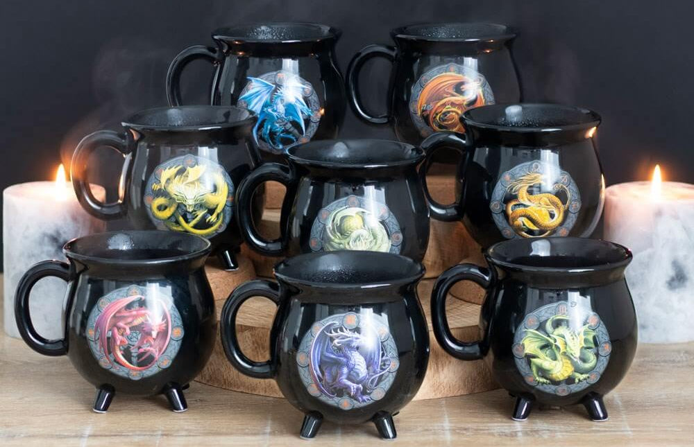 Set of black mugs with dragon designs on a wooden surface with candles in the background.