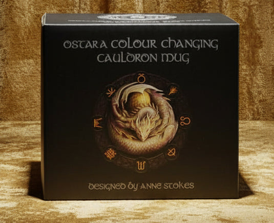 A black product box for the Ostara Colour Changing Cauloron Mug, featuring a detailed illustration of a snake wrapped around a mug and white text, on a plain white background.