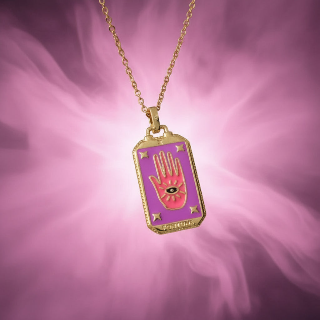 Gold necklace with a purple pendant featuring a hand design on a textured beige surface