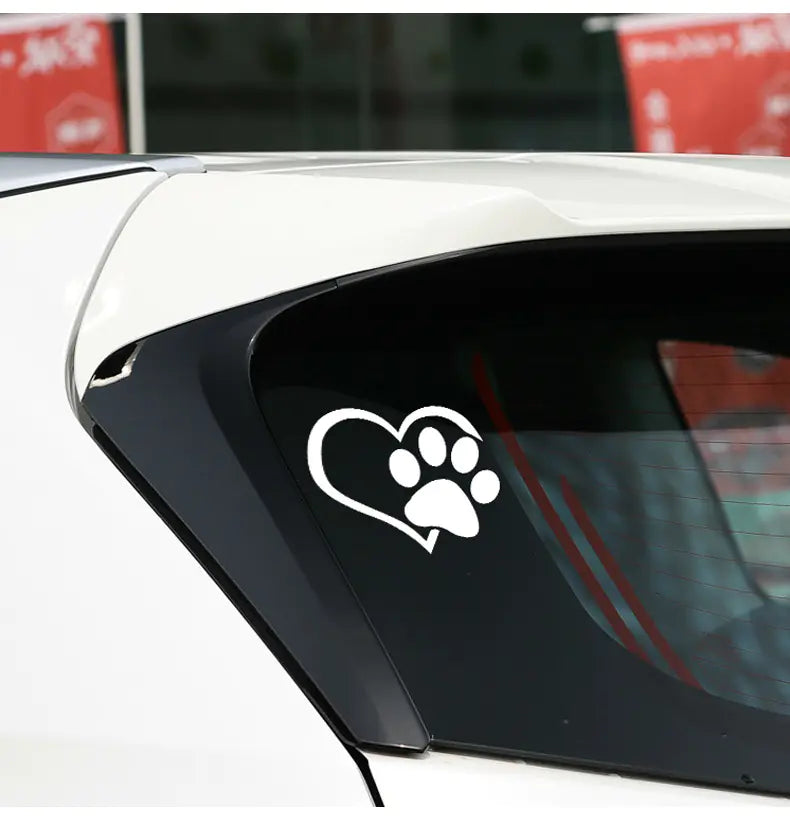 Car window with a white paw print heart decal on a blurred background