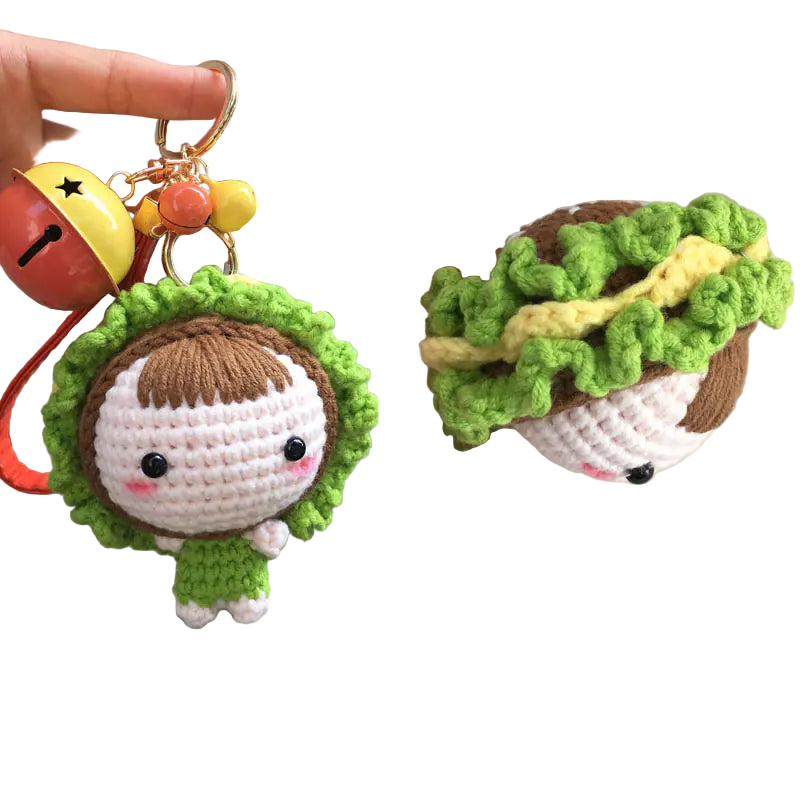 Crocheted keychain with a character wearing a green hat and holding a yellow bell, close-up of the character.