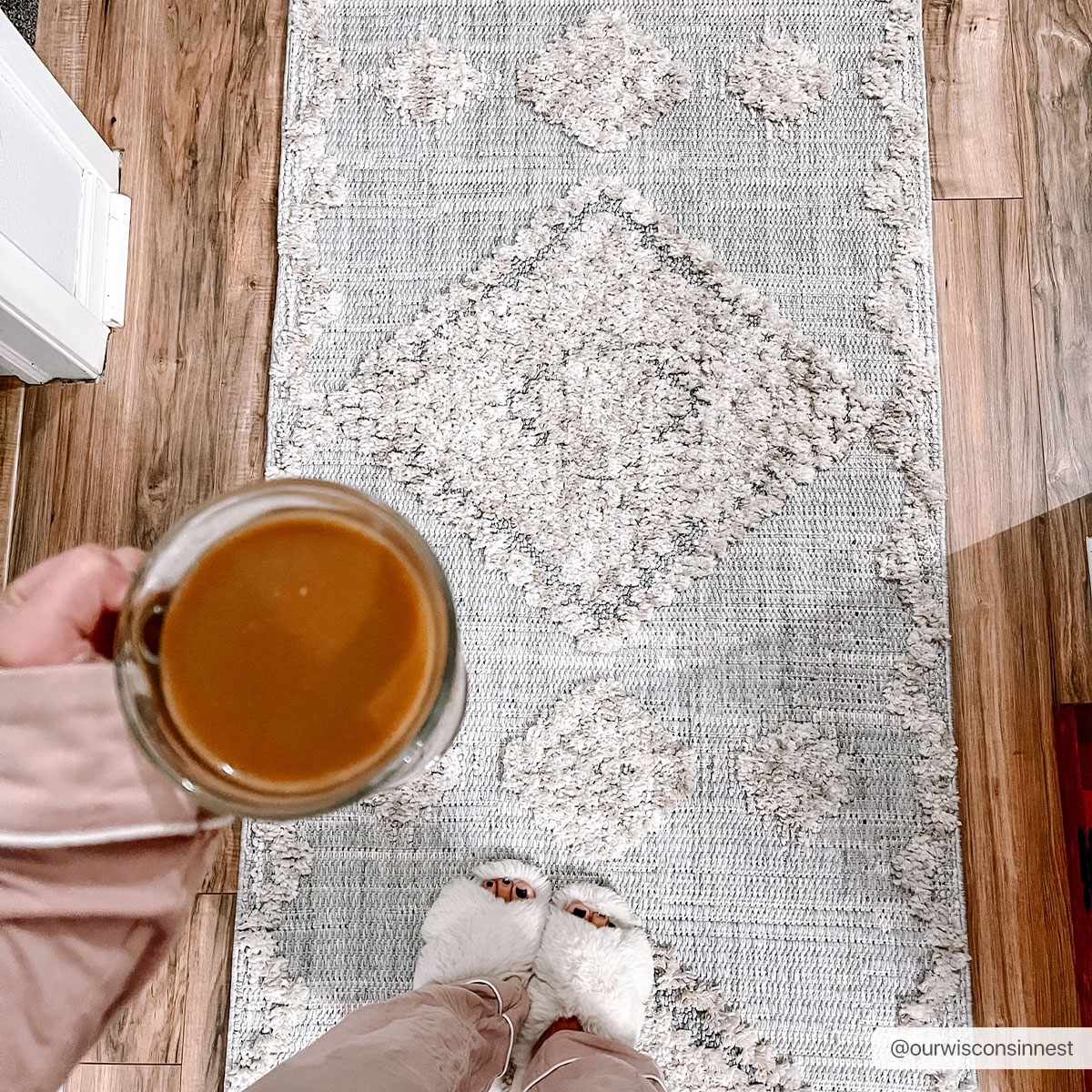 Person holding a mug of coffee on a patterned rug