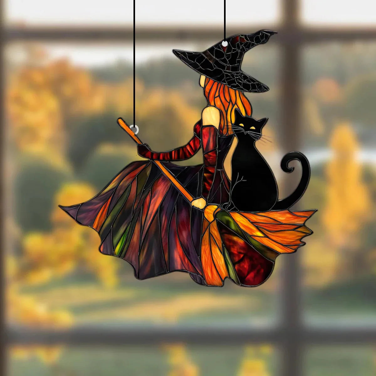 Decorative stained glass witch and black cat on a broom hanging against a blurred autumn window background.