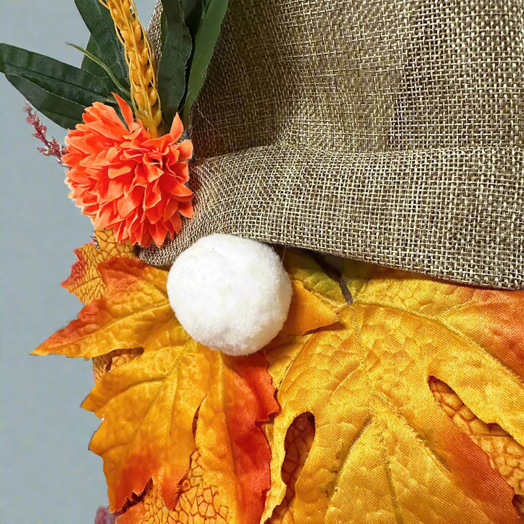 Decorative wreath with autumn leaves, flowers, and a white pom-pom on a plain background