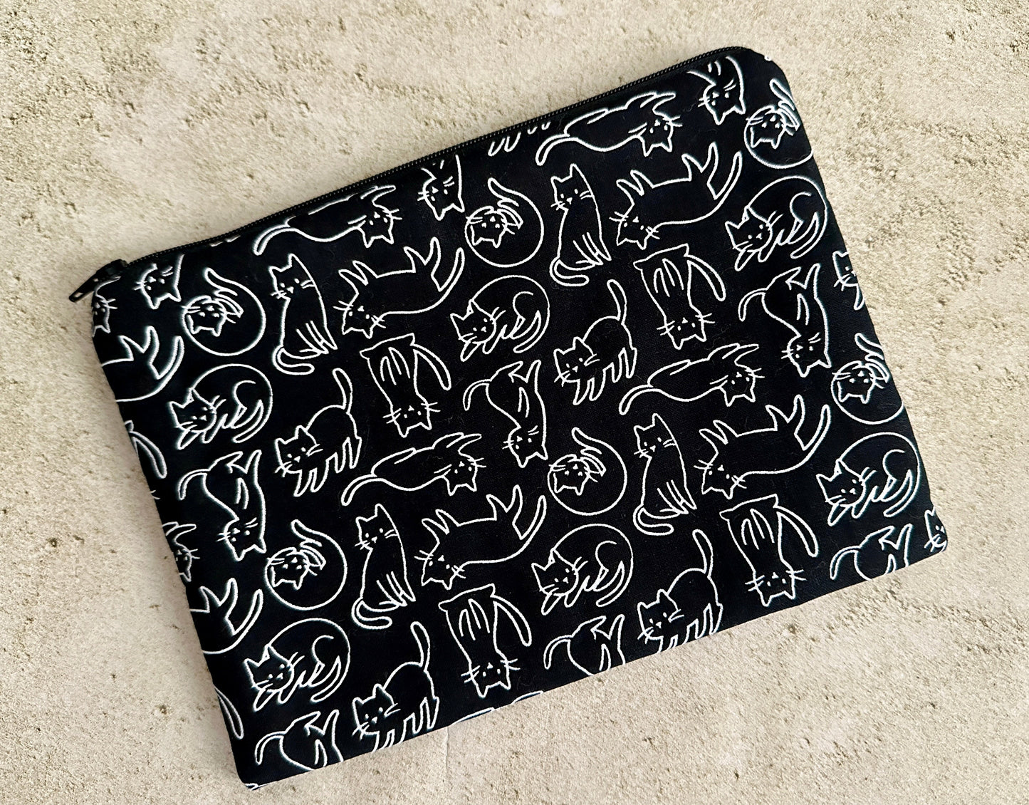 Black pouch with white cat pattern on a beige surface