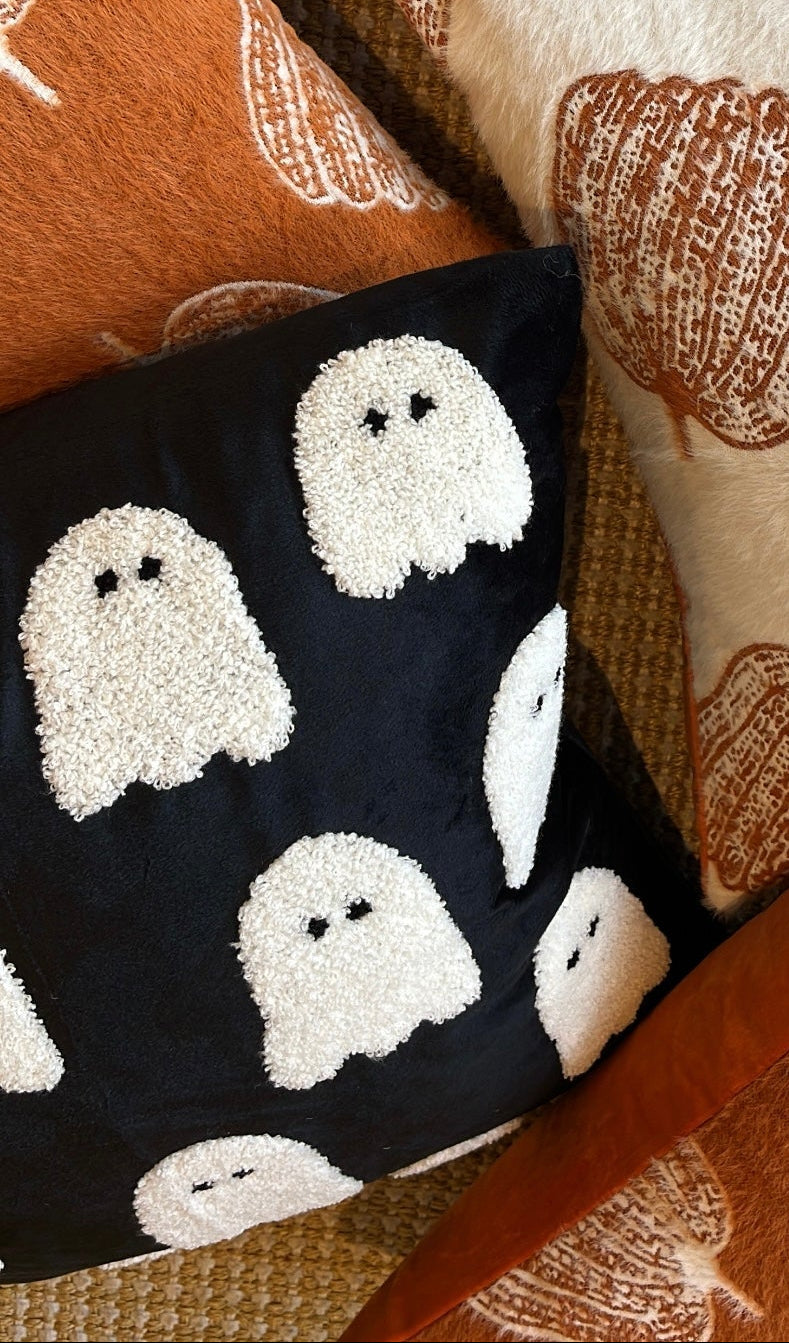 Decorative pillows with pumpkin and ghost patterns on a textured surface.