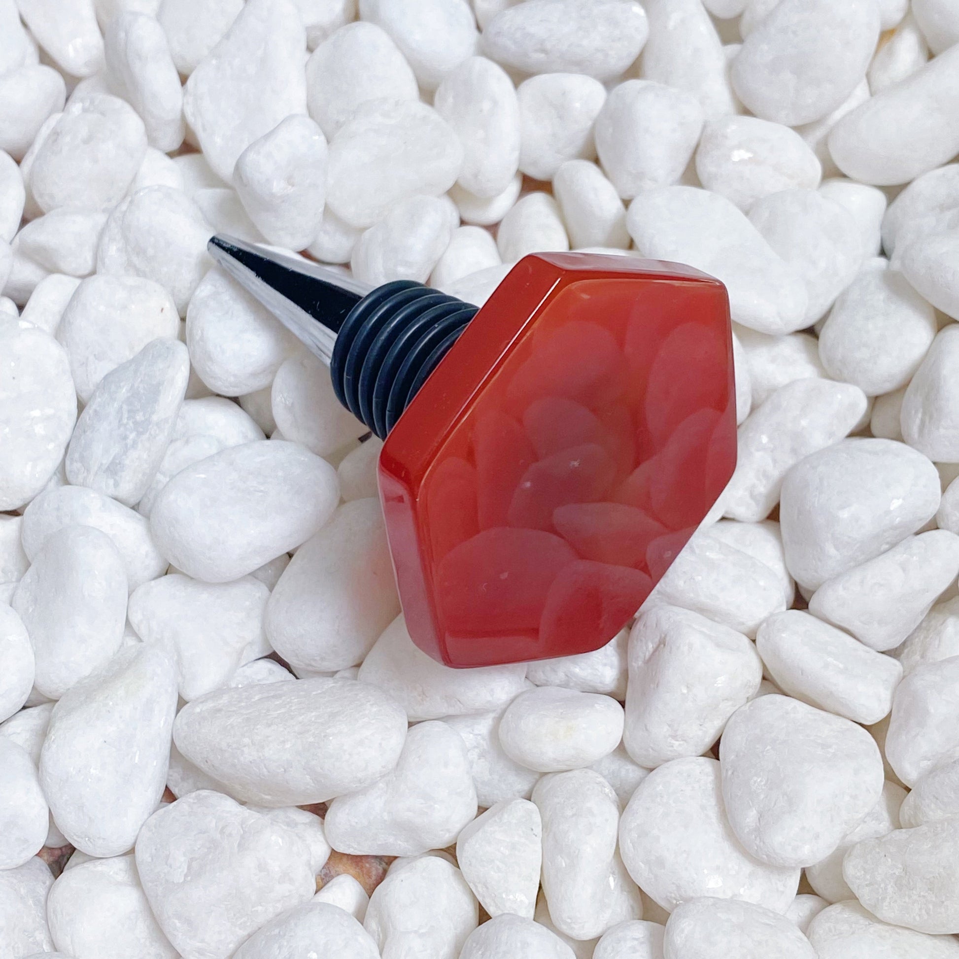 Red bottle stopper with black cap on white pebbles