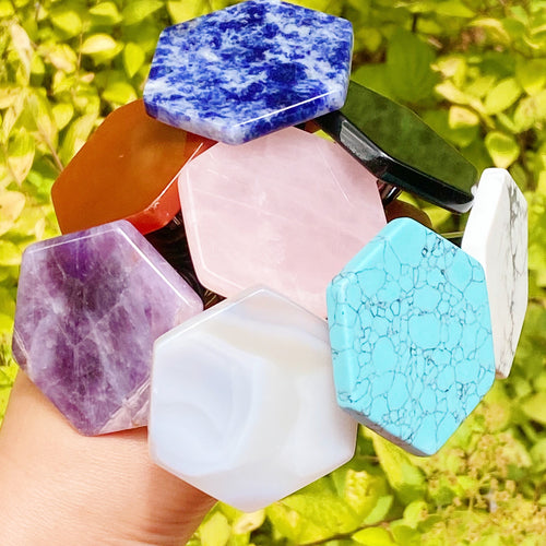 Colorful hexagonal stone beads held by a hand with a green leafy background