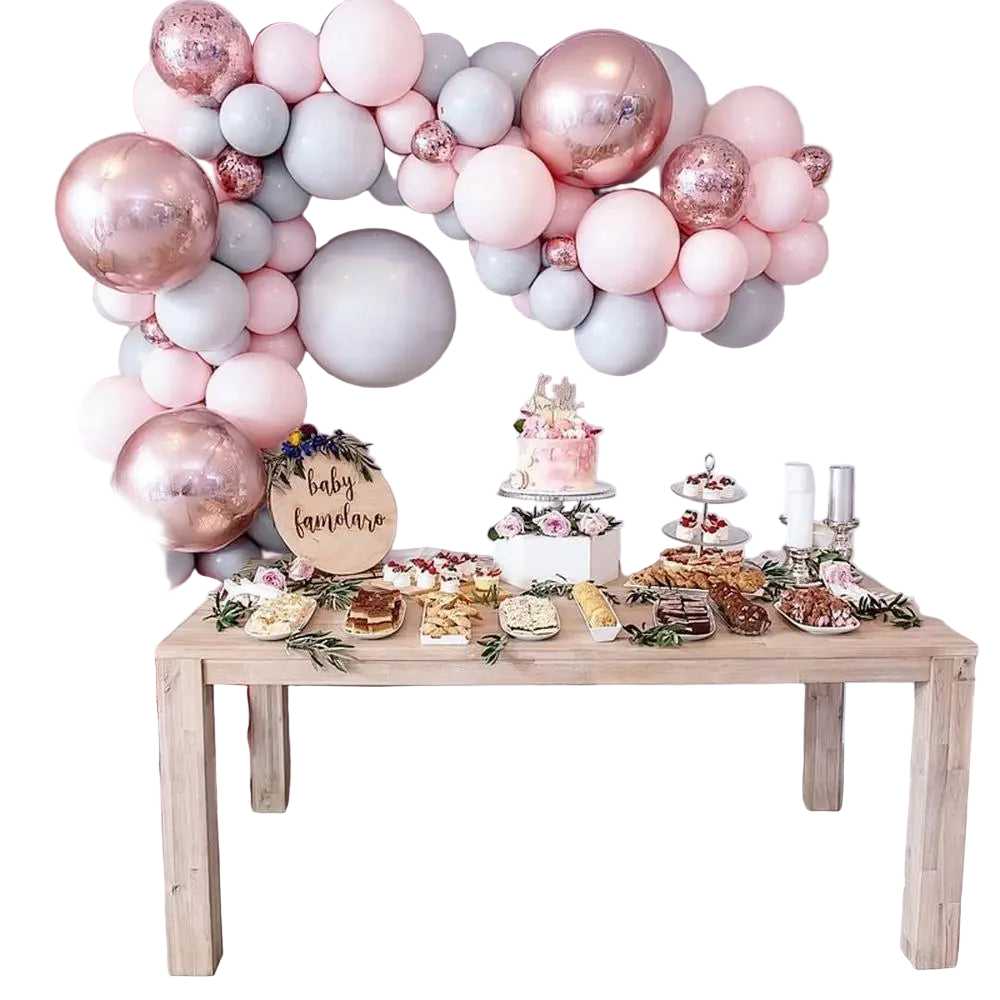 Decorative balloon arch with a baby shower setup including a cake and pastries on a table.