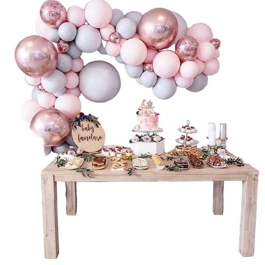 Decorative balloon arch with a baby shower setup including a cake and pastries on a table.
