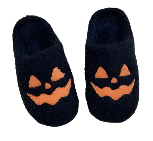 Black slippers with jack-o'-lantern faces on a white blanket