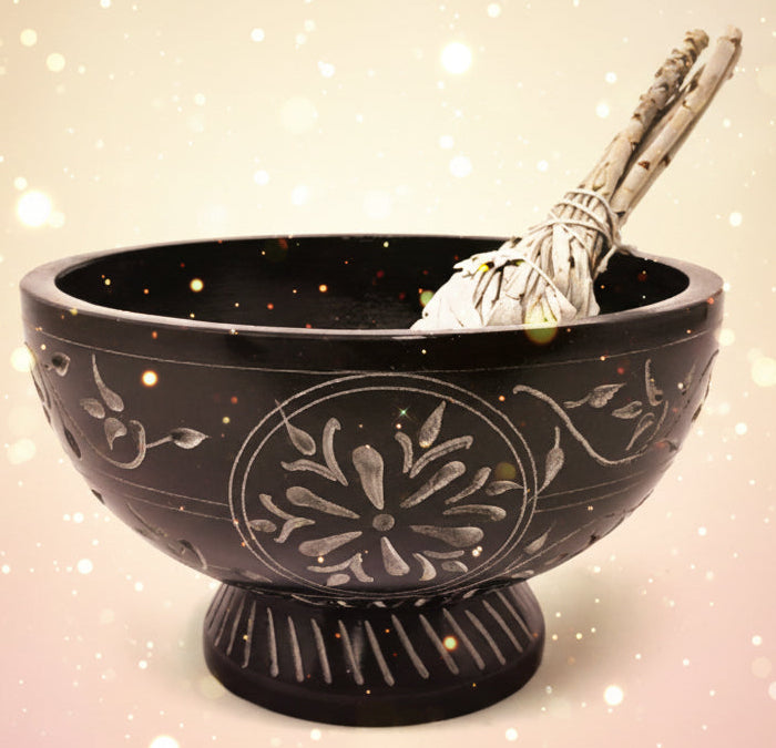 Black decorative bowl with floral patterns and a silver spoon on a white background