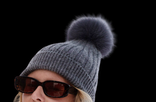 Woman wearing a gray knit beanie with a black pom-pom and sunglasses on a white background
