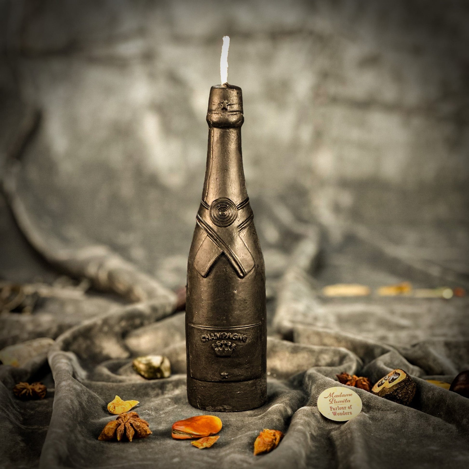 Bronze bottle-shaped candle with a lit wick on a textured surface with dried flowers.