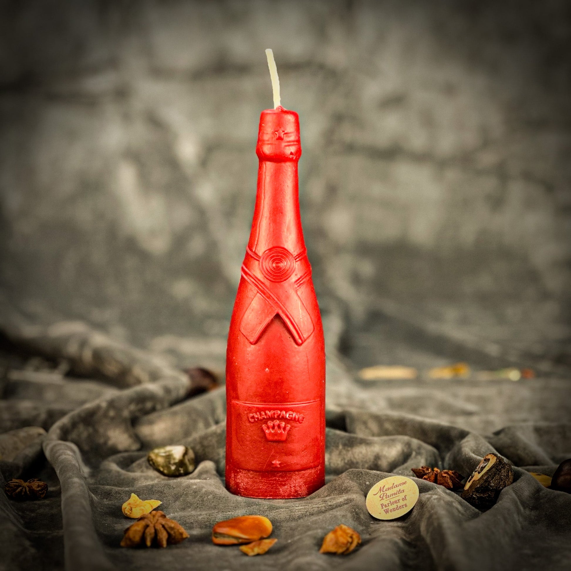 Red bottle-shaped candle with 'Olympea' branding on a textured surface.