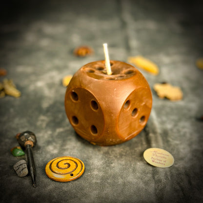 Wooden dice-shaped candle with a lit wick on a dark surface with decorative items.
