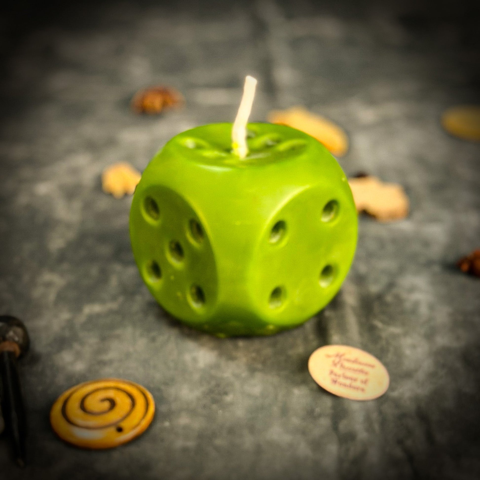 Green dice-shaped candle on a dark surface with small objects around