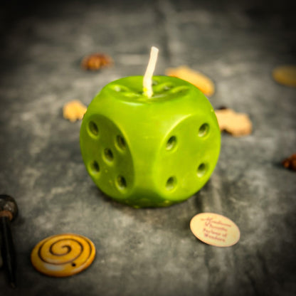 Green dice-shaped candle on a dark surface with small objects around
