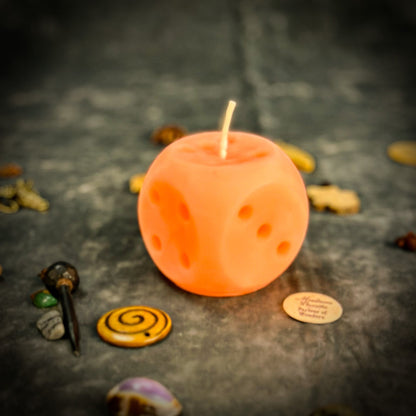 Orange candle shaped like a dice with small stones and a spiral on a dark surface