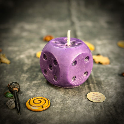 Purple dice-shaped candle on a dark surface with small decorative items around it