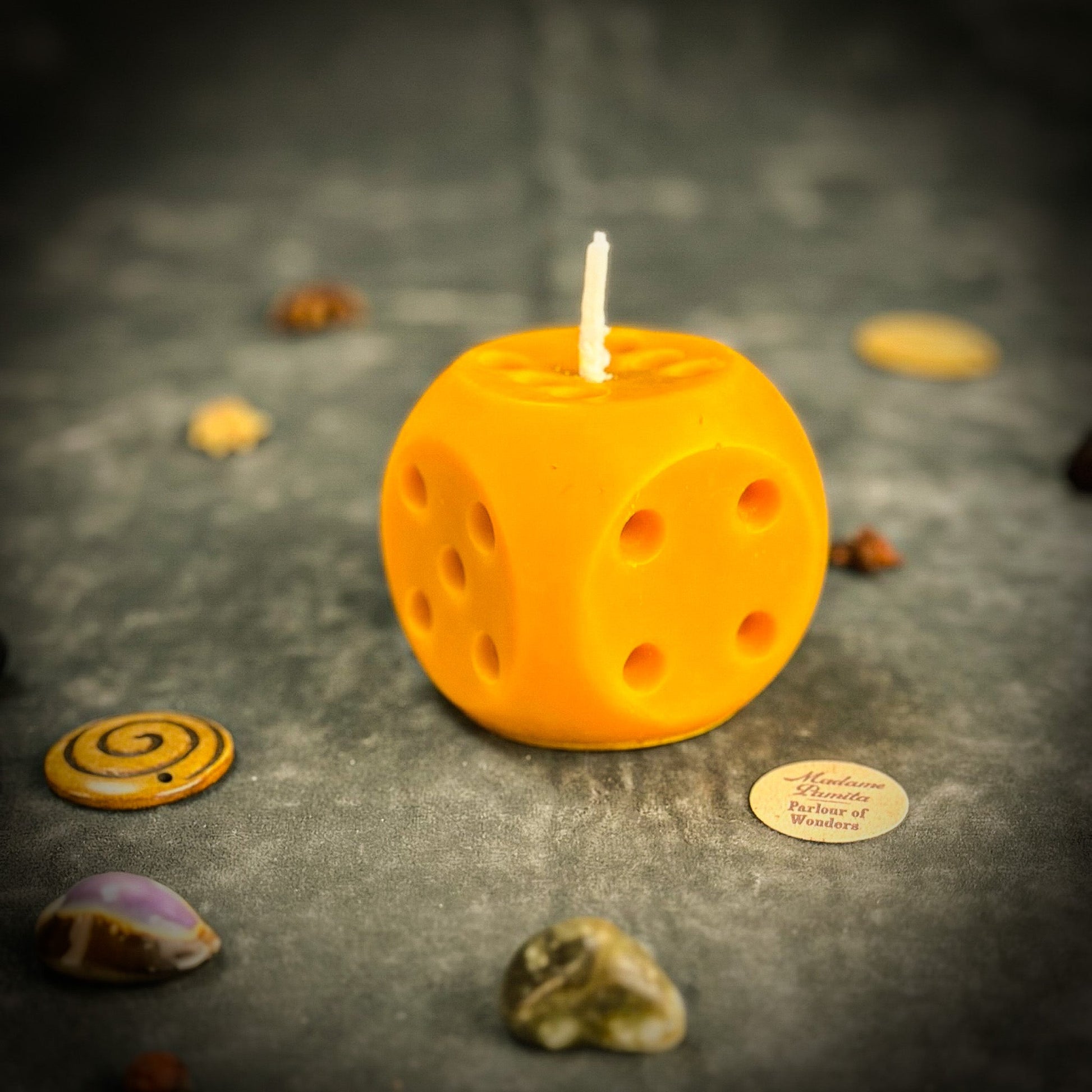 Yellow dice-shaped candle on a dark surface with decorative stones.