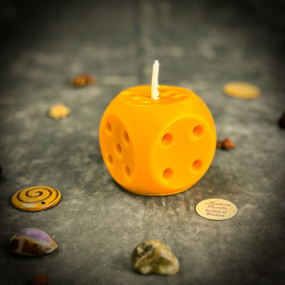 Yellow dice-shaped candle on a dark surface with decorative stones.