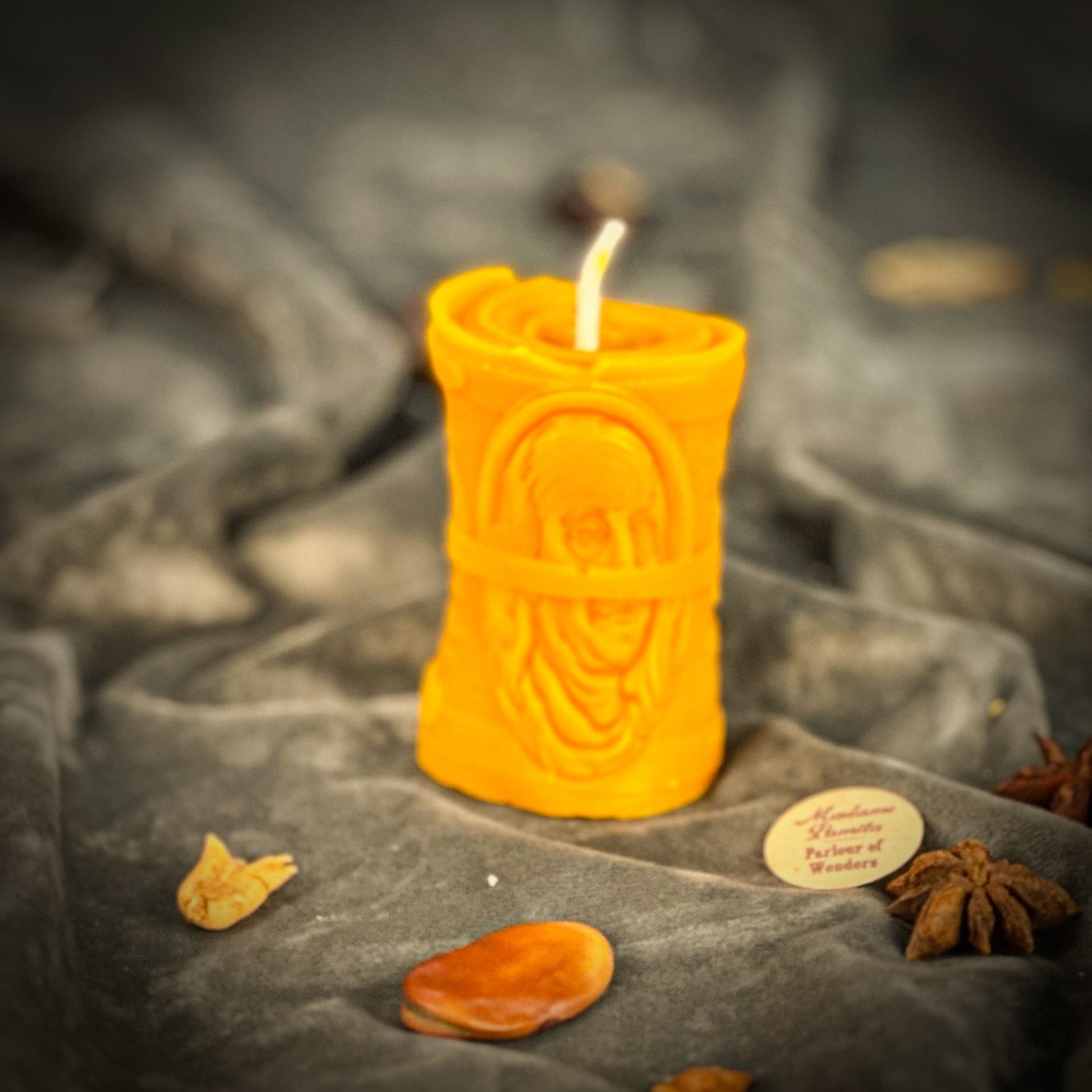 Decorative candle with intricate design on a stone surface with dried fruits and spices.