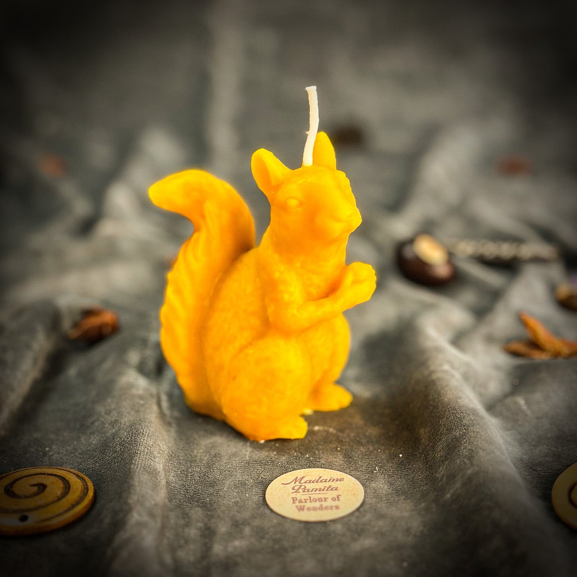 Yellow squirrel-shaped candle on a textured surface with a brand label.